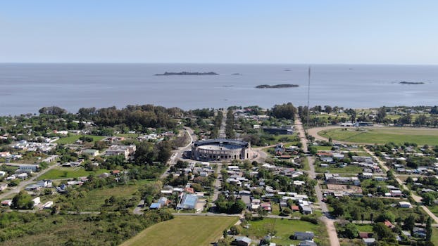 Aerial view of Colonia Del Sacramento, featuring the coast and Plaza de Toros with lush greenery.