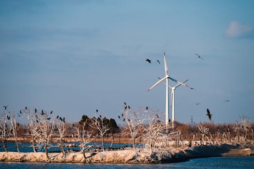 Scenic view of wind turbines with birds perched on trees and flying in a tranquil landscape.