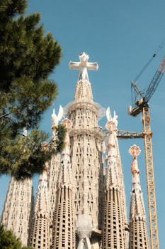 View of Sagrada Familia's intricate towers with construction crane on a sunny day in Barcelona.